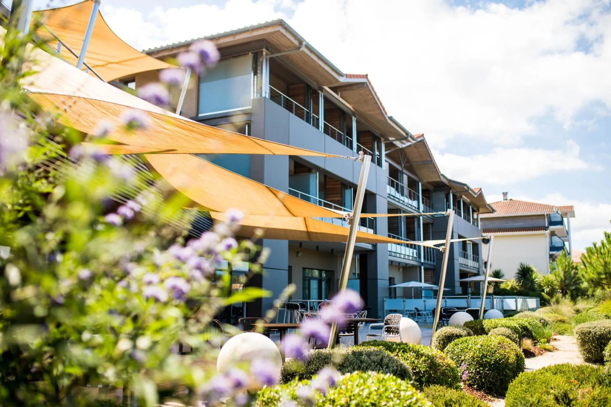 Bâtiment moderne avec des terrasses ombragées et une végétation luxuriante.