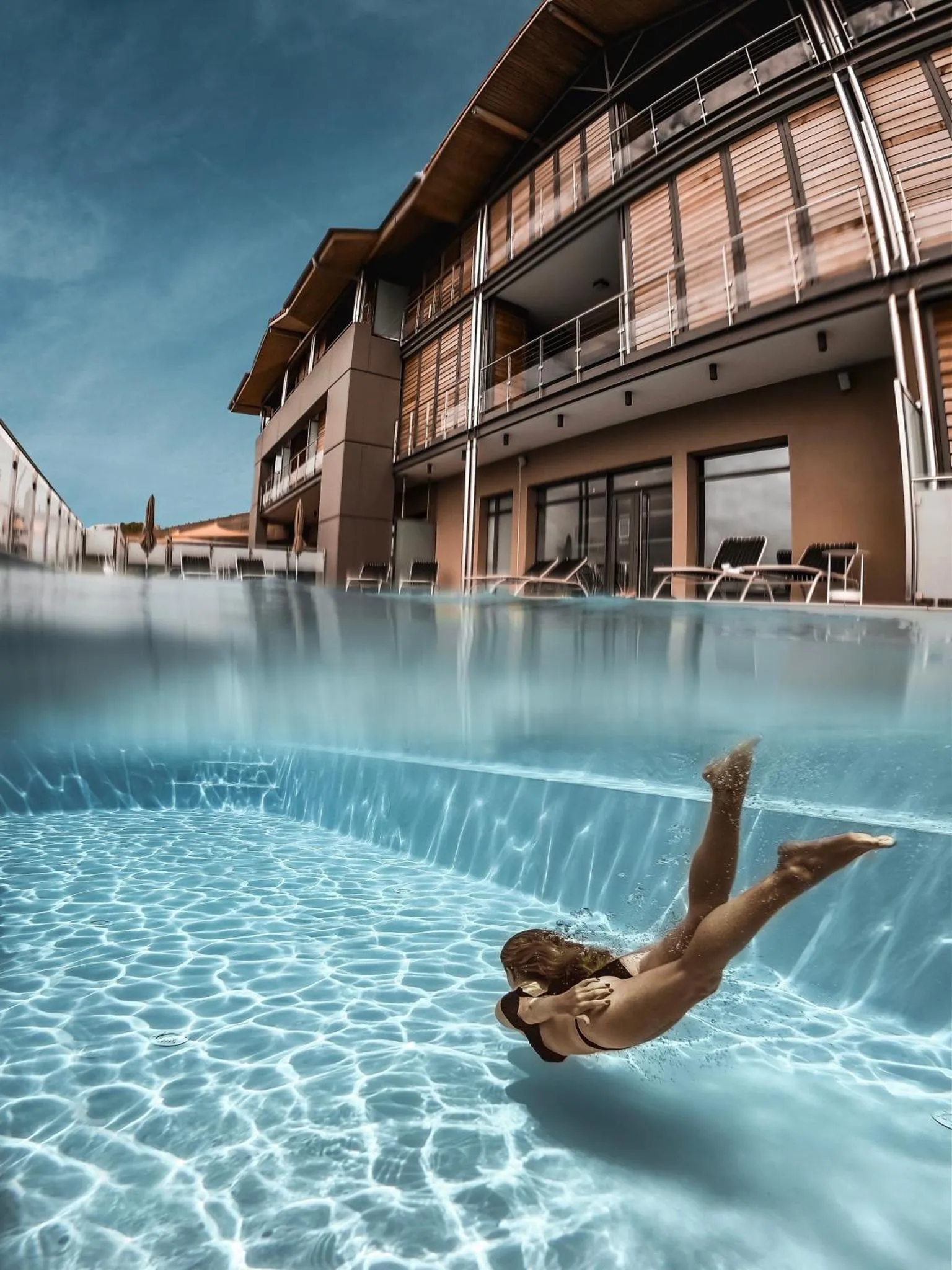 Une personne nage sous la surface d'une piscine devant un bâtiment moderne.
