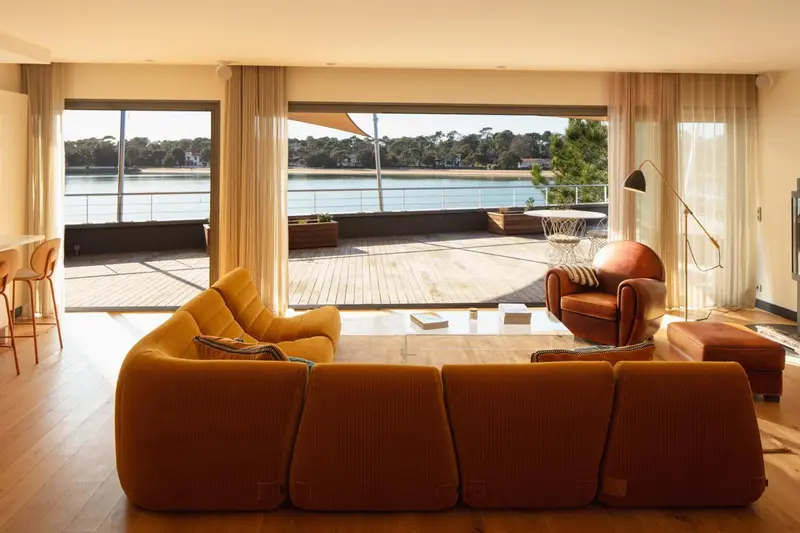 Un salon lumineux s'ouvre sur une terrasse en bois avec vue sur l'eau.