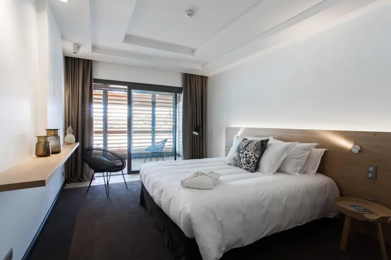 Chambre lumineuse avec un grand lit et un accès à une terrasse.