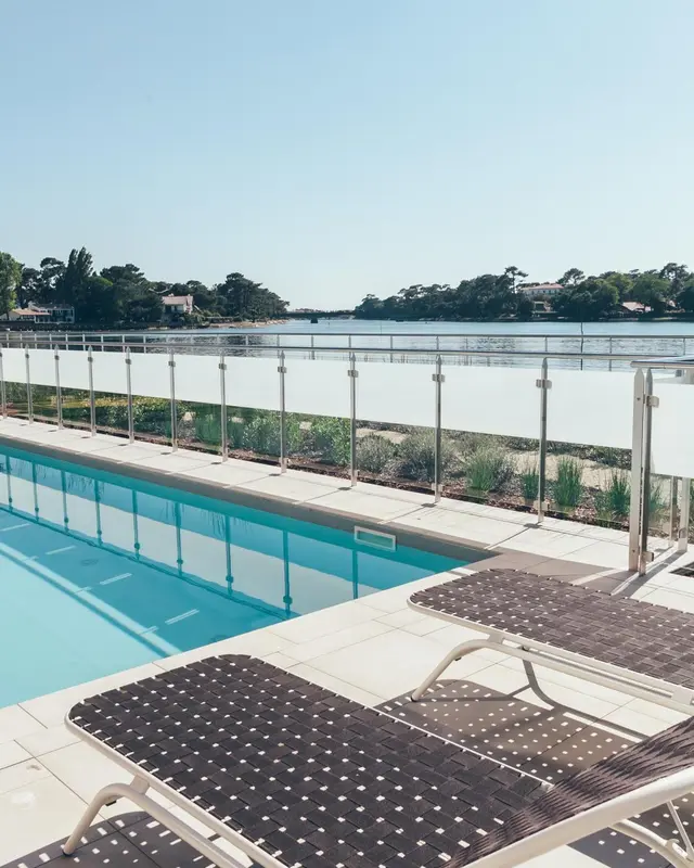 Transats et piscine bordée d'une rambarde en verre avec vue sur la mer.