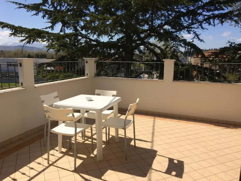 Une table et des chaises blanches sont disposées sur une terrasse carrelée ensoleillée.