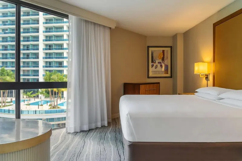 Chambre lumineuse avec un grand lit et une vue sur la mer et une piscine.