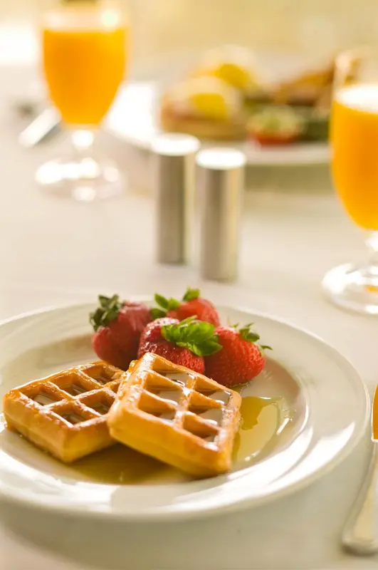 Une table est dressée avec un petit-déjeuner composé de gaufres, de fraises et de jus d'orange.