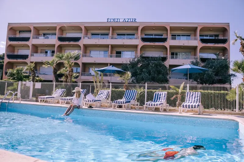 Bâtiment beige avec des balcons et des transats bleus et blancs près d'une piscine.
