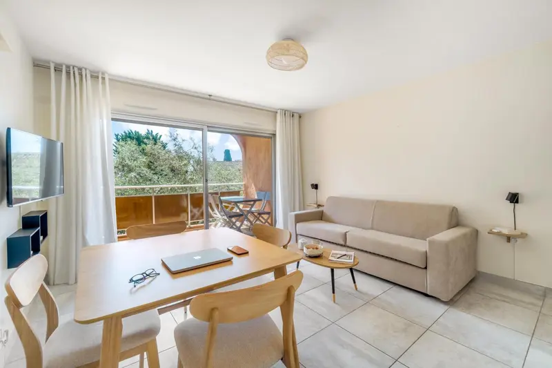 Espace de vie lumineux avec canapé et table à manger près d'une baie vitrée.