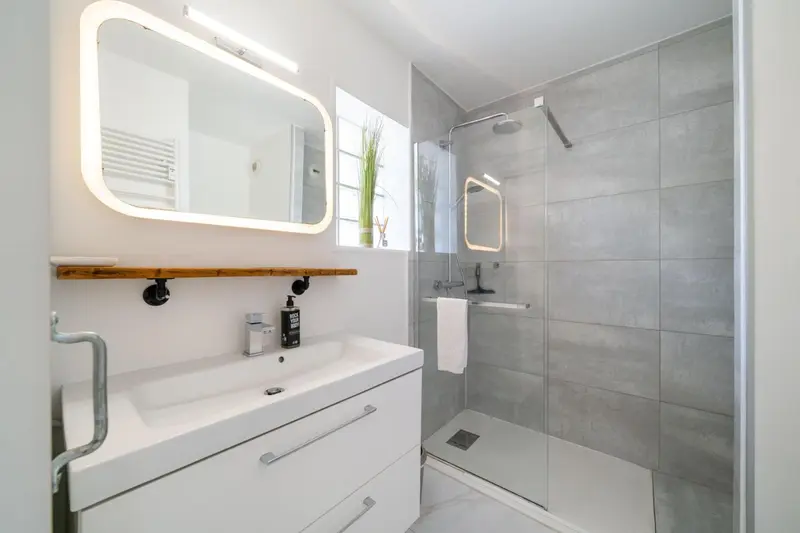 Une salle de bain moderne avec douche à l'italienne et grand miroir lumineux.