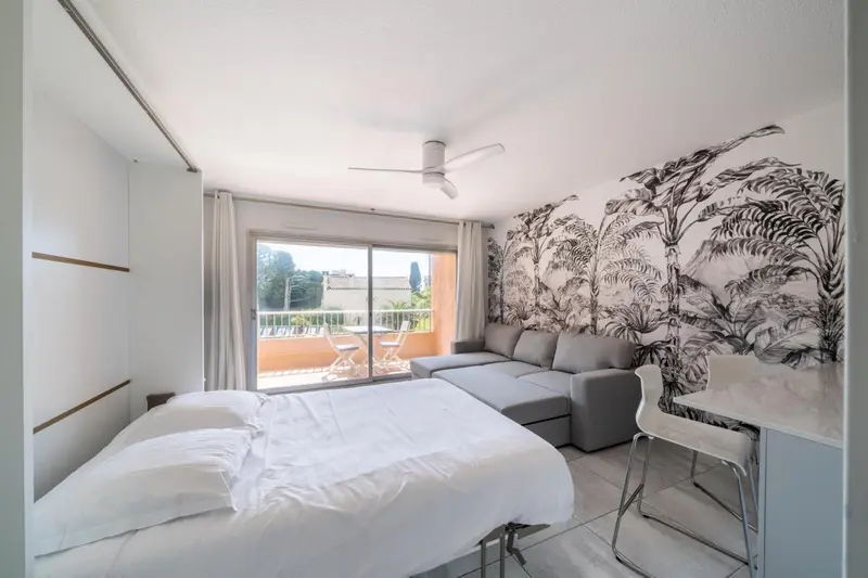 Une chambre lumineuse avec un canapé d'angle et un accès à un balcon.