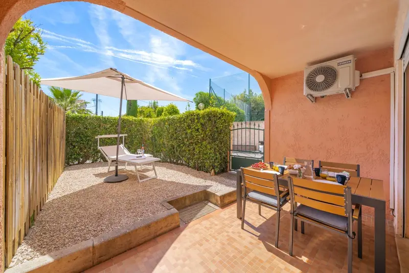 Une terrasse ombragée donne sur une cour avec mobilier de jardin et une table à manger.