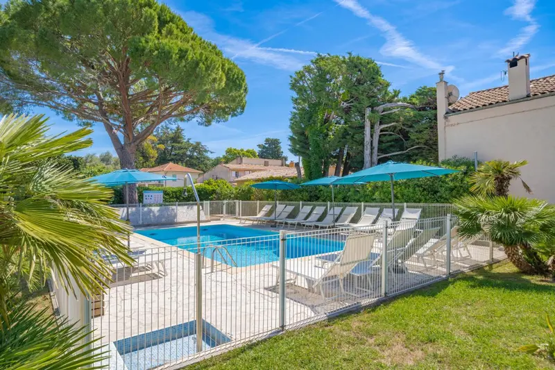 Piscine ensoleillée entourée de chaises longues et de végétation luxuriante.