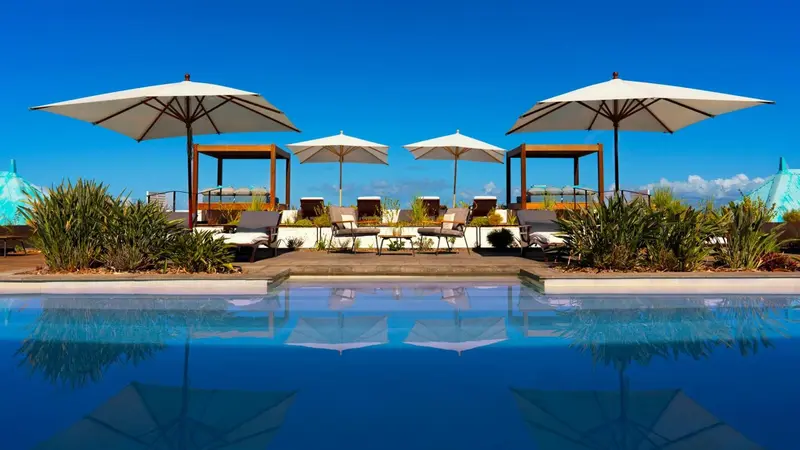 Transats et parasols bordent une piscine d'eau claire sous un ciel bleu.
