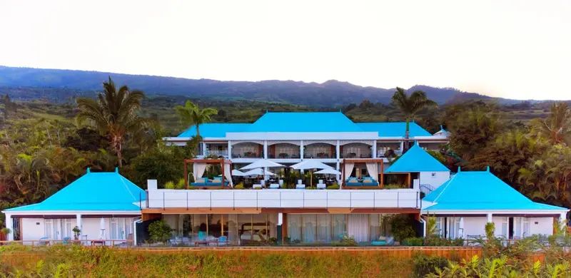 Bâtiment bleu turquoise avec des palmiers et des montagnes en arrière-plan.