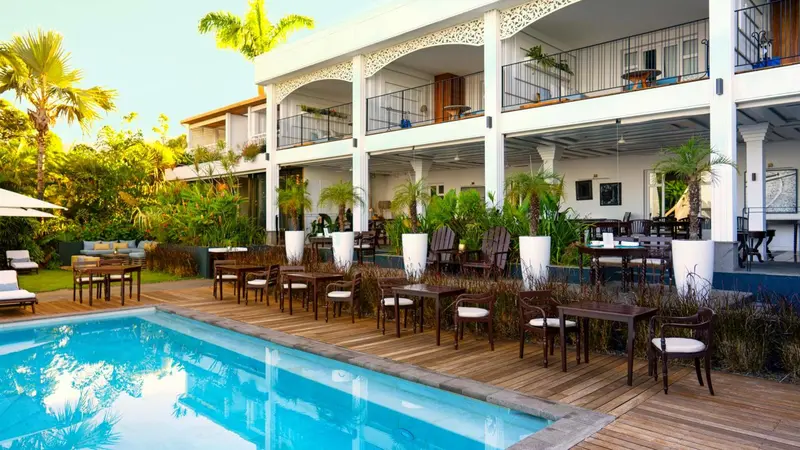 Terrasse avec tables et chaises près d'une piscine et d'un bâtiment blanc.
