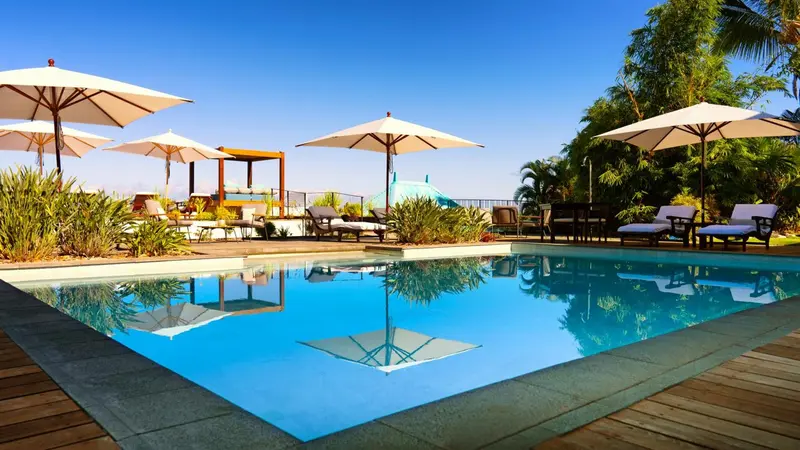 Une piscine rectangulaire bordée de transats sous des parasols blancs.