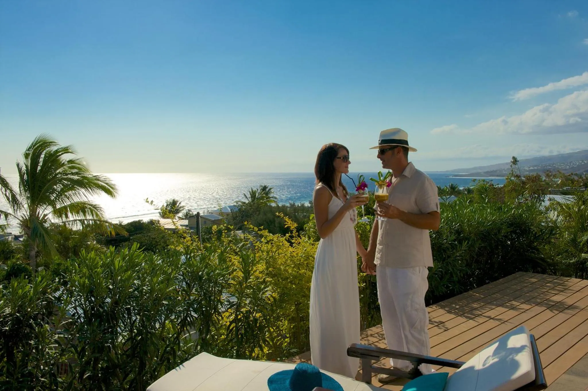Un couple trinque avec des cocktails sur une terrasse ensoleillée avec vue sur la mer.