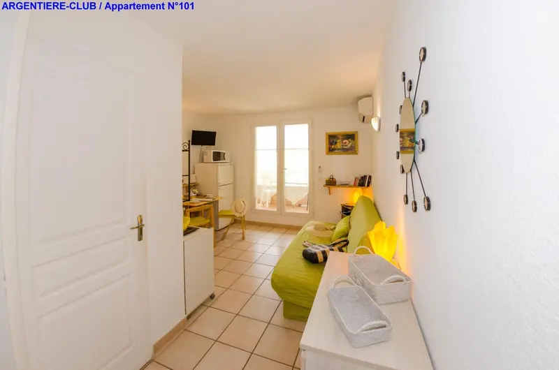 Une piece de vie lumineuse avec un canape vert et une kitchenette.