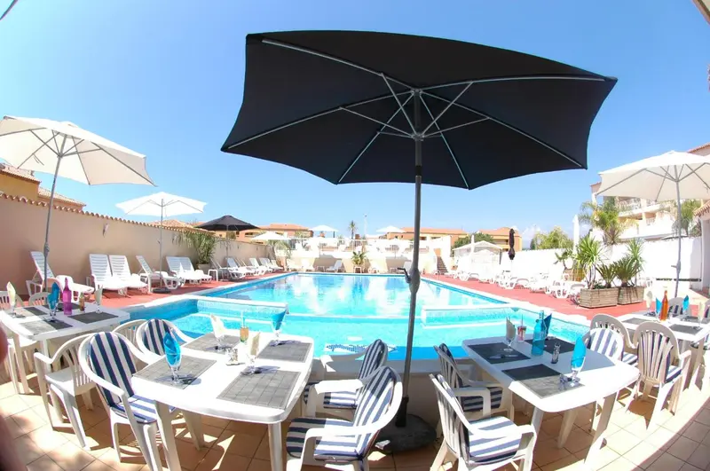 Terrasse avec tables et chaises près d'une piscine ensoleillée.