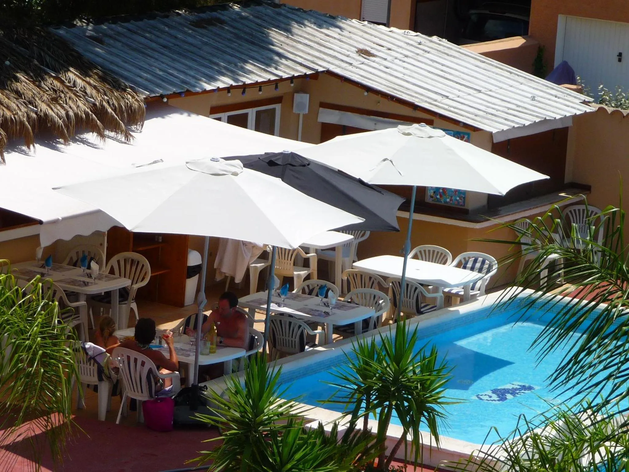Terrasse ombragée avec tables et chaises près d'une piscine.