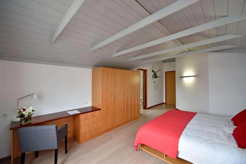 Une chambre lumineuse avec un bureau et un lit recouvert d'une couverture rouge.
