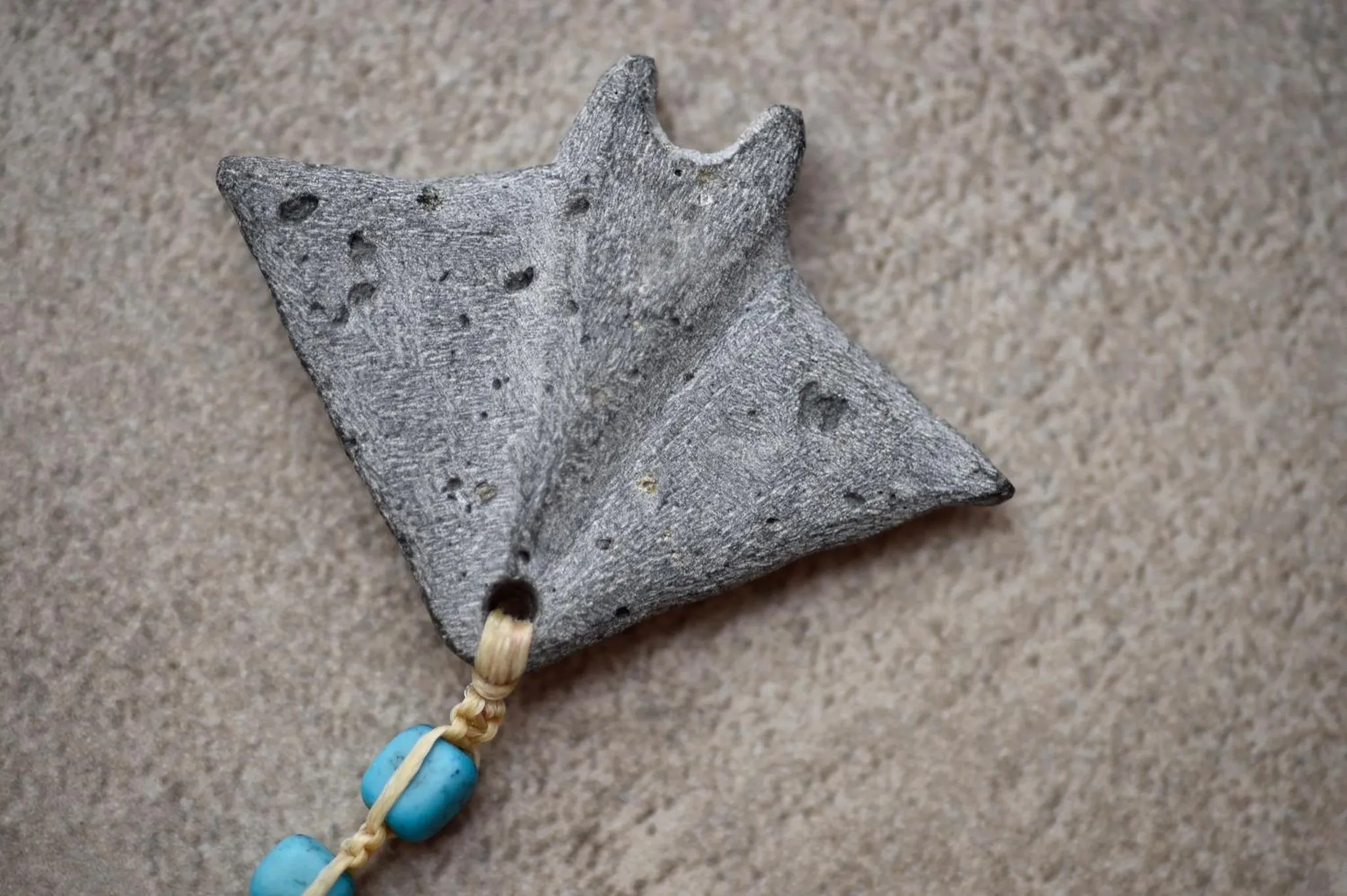 Un objet sculpté en forme de raie manta repose sur une surface sableuse.