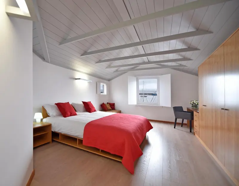 Une chambre lumineuse avec un lit rouge et un bureau près d'une fenêtre.