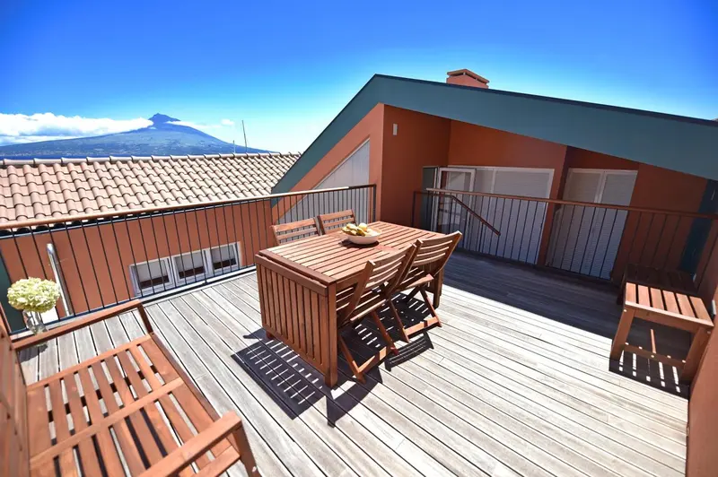 Terrasse en bois avec table et chaises, vue sur un paysage montagneux.