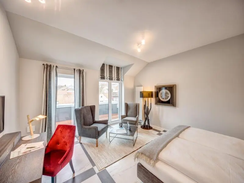 Une chambre lumineuse avec un bureau, deux fauteuils et un lit.