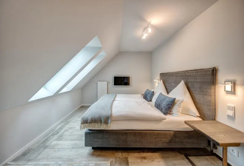 Une chambre mansardée avec un grand lit et des oreillers décoratifs.