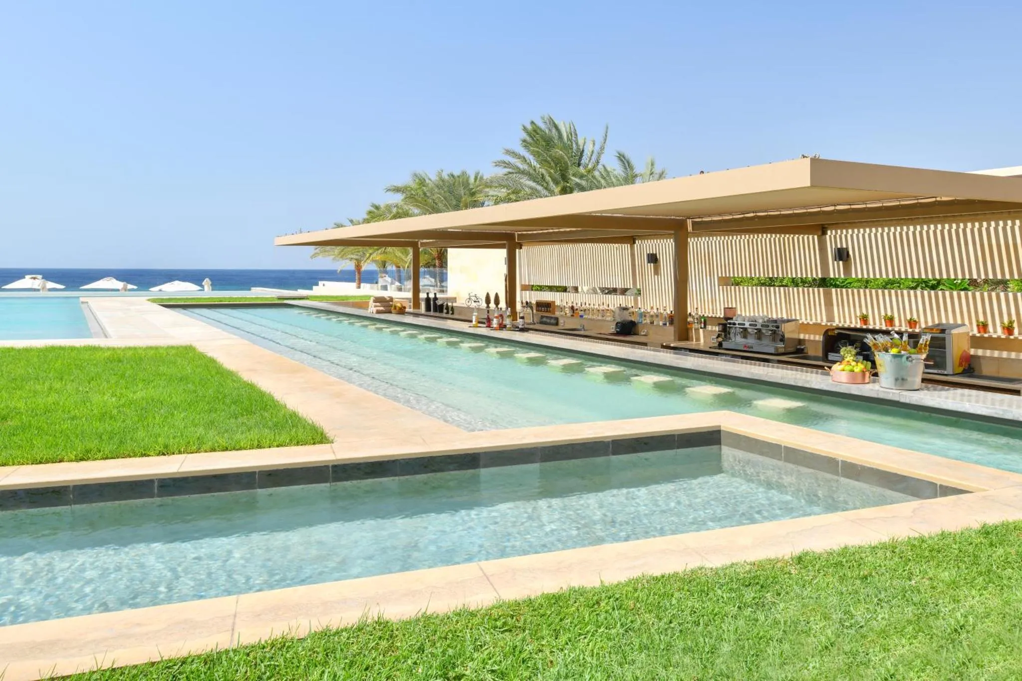 Terrasse ombragée avec piscine et végétation luxuriante en bord de mer.