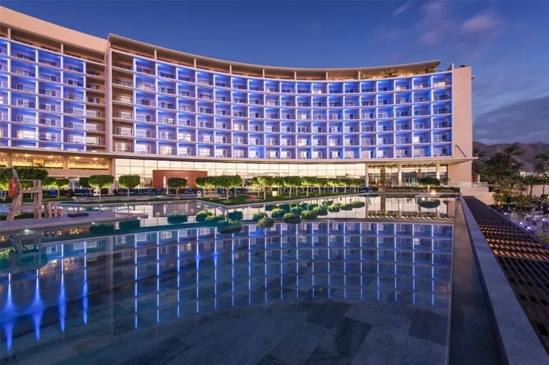 Bâtiment moderne illuminé reflété dans une piscine calme au crépuscule.