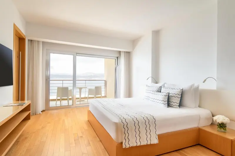 Chambre lumineuse avec un grand lit et un balcon donnant sur la mer.
