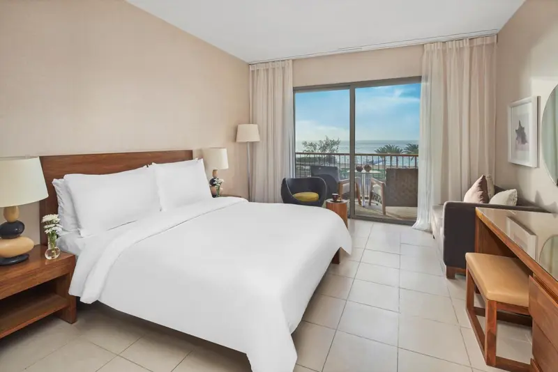Une chambre lumineuse avec un grand lit et un balcon offrant une vue sur la mer.