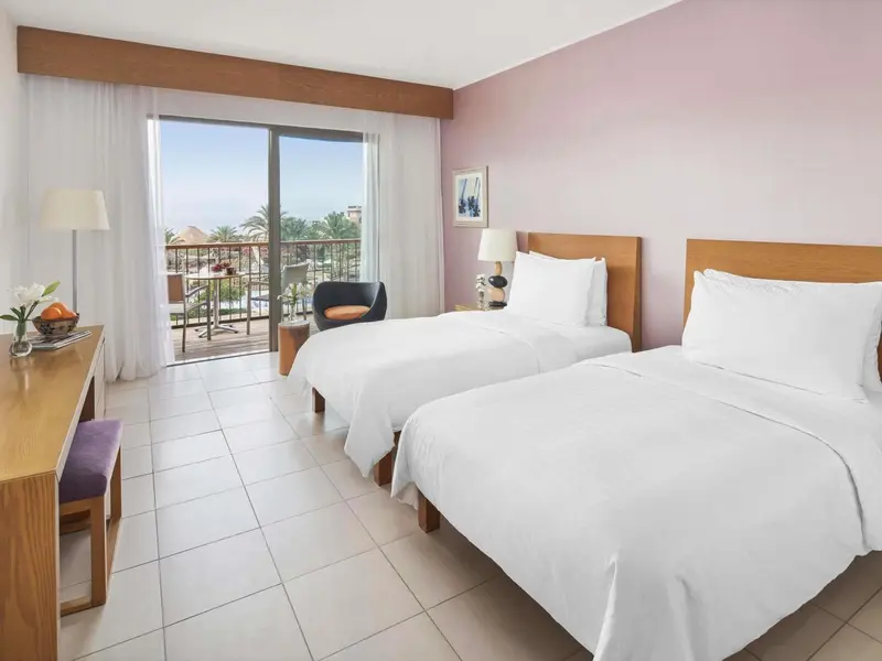 Chambre lumineuse avec deux lits simples et vue sur la mer.