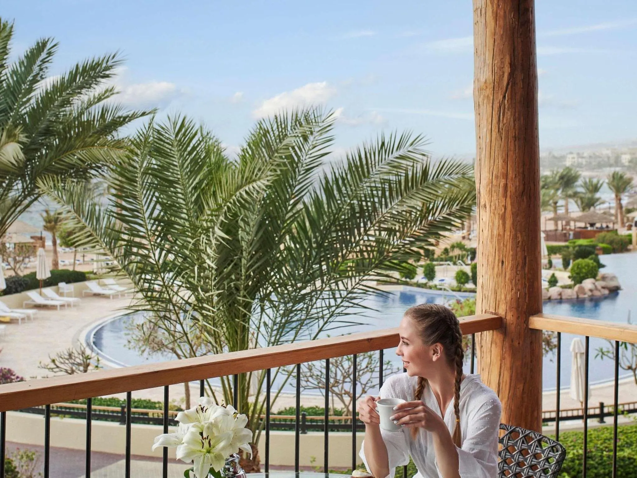 Une femme assise sur une terrasse en bois, face à une vue sur la mer et une piscine.
