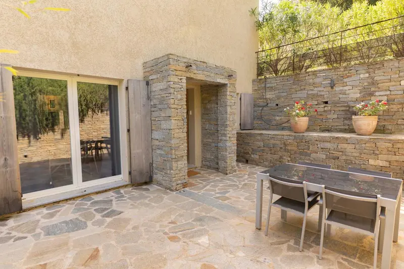 Terrasse pavée avec table et chaises devant une entrée en pierre.