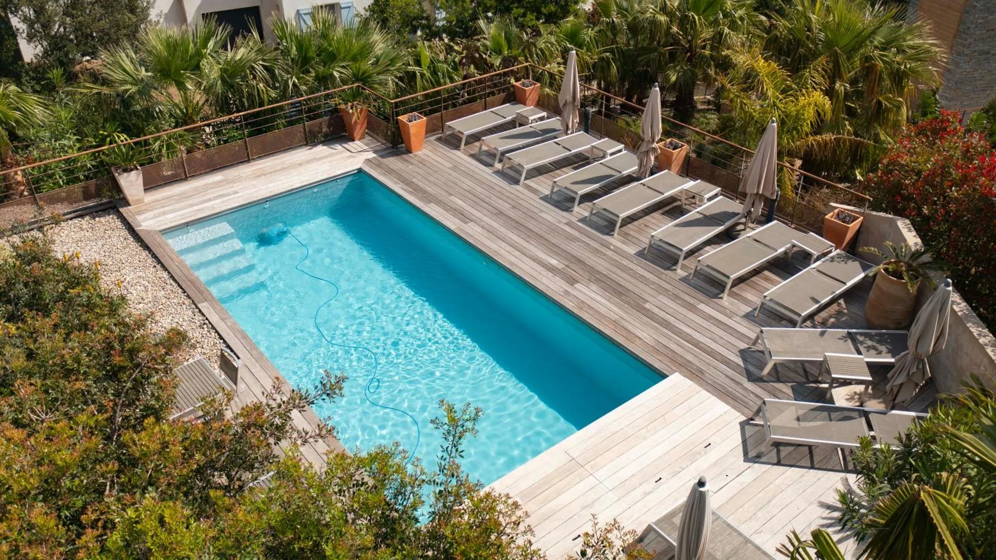 Une piscine rectangulaire entourée d'une terrasse en bois avec des transats.