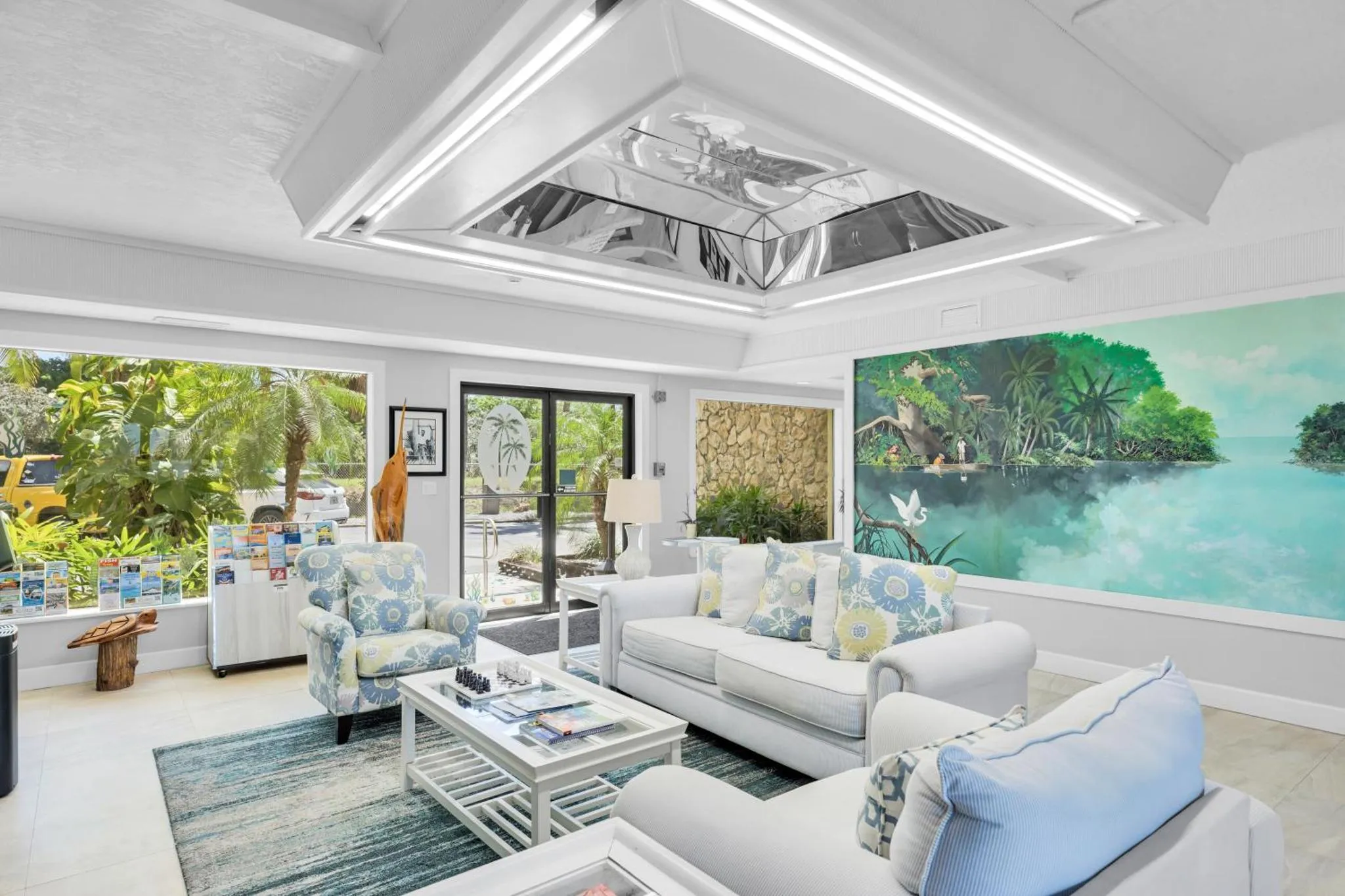 Espace de détente lumineux avec canapés confortables et une grande fresque murale représentant un paysage tropical.