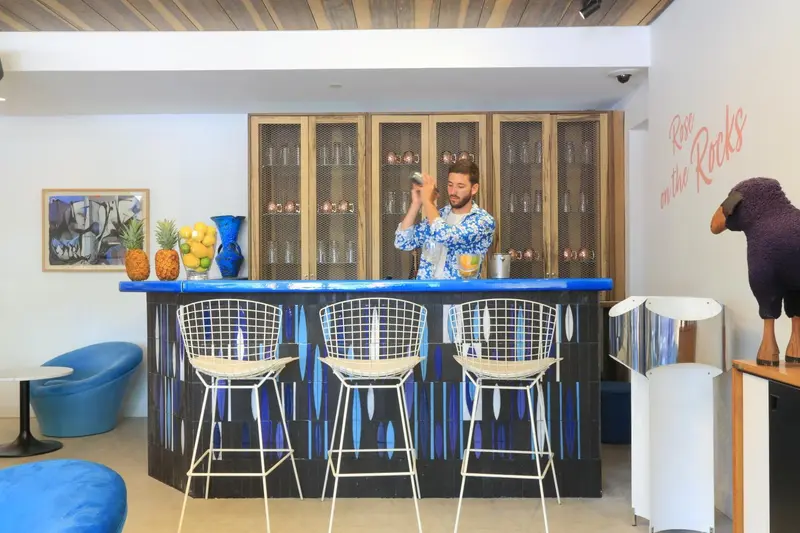 Un barman prépare un cocktail devant un comptoir bleu et des étagères à bouteilles.