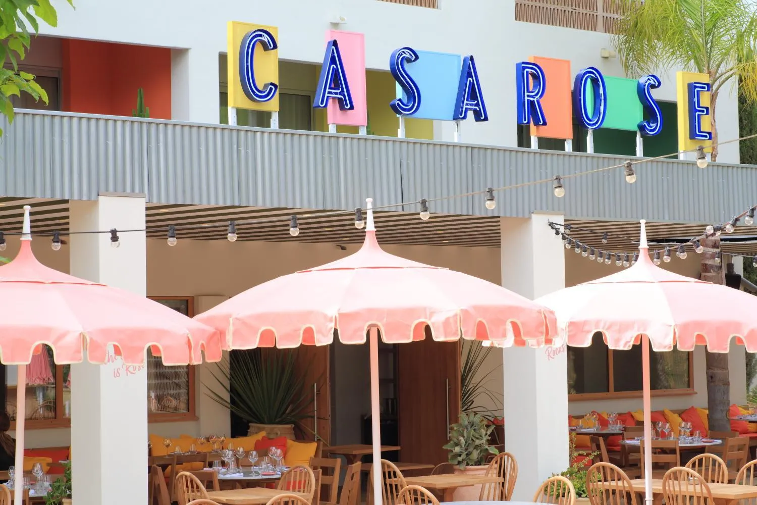 Terrasse ombragée avec des parasols roses et des tables de restaurant.
