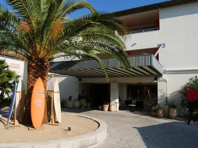 Façade d'un bâtiment blanc avec des planches de surf et une végétation luxuriante.