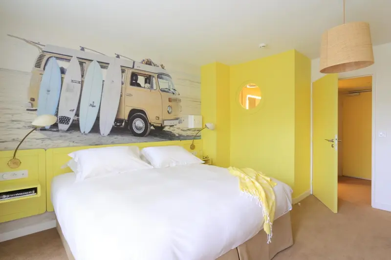 Une chambre lumineuse avec un lit blanc et une décoration murale sur le thème du surf.