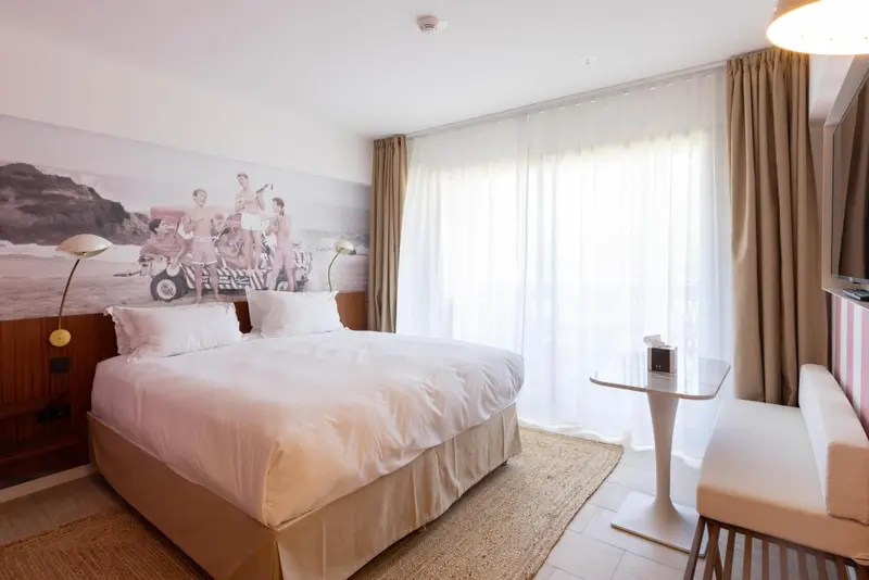 Une chambre lumineuse avec un grand lit et une décoration murale représentant une scène de plage.
