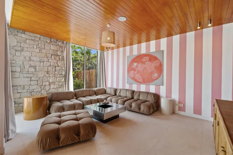 Un salon moderne avec un canapé d'angle et un mur rayé rose et blanc.
