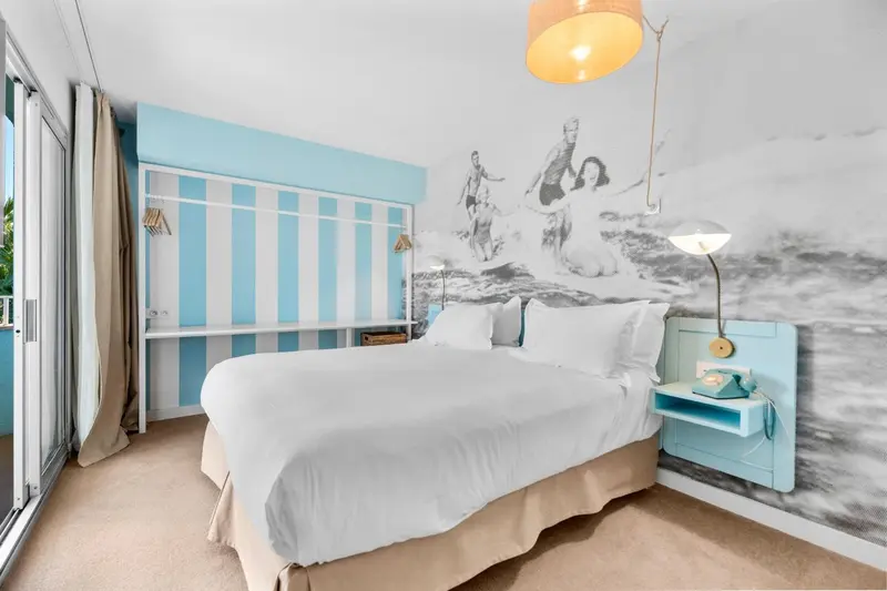Une chambre lumineuse avec un grand lit et un mur décoratif représentant des silhouettes nautiques.