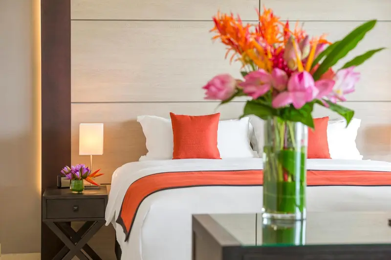 Un lit avec une couverture orange et des oreillers blancs est décoré de fleurs tropicales.