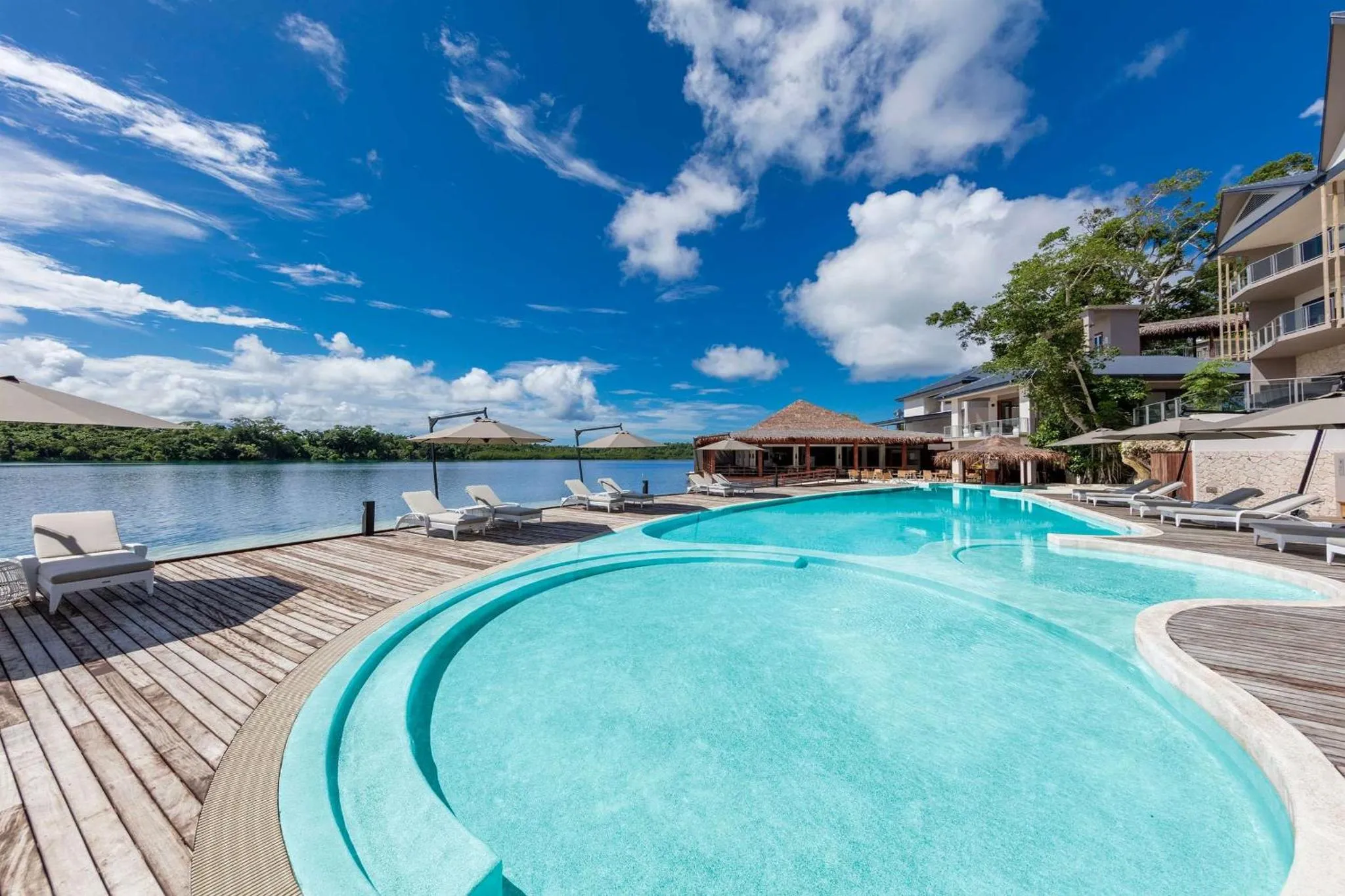 Une piscine turquoise bordée d'une terrasse en bois avec des transats et des parasols.