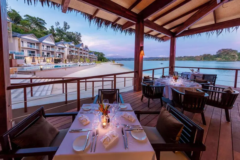 Tables dressées pour un dîner en extérieur avec vue sur la mer au coucher du soleil.