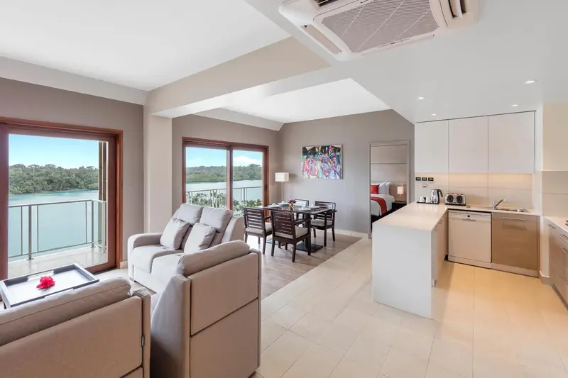 Espace de vie lumineux avec canapés, table à manger et cuisine équipée donnant sur une vue dégagée.