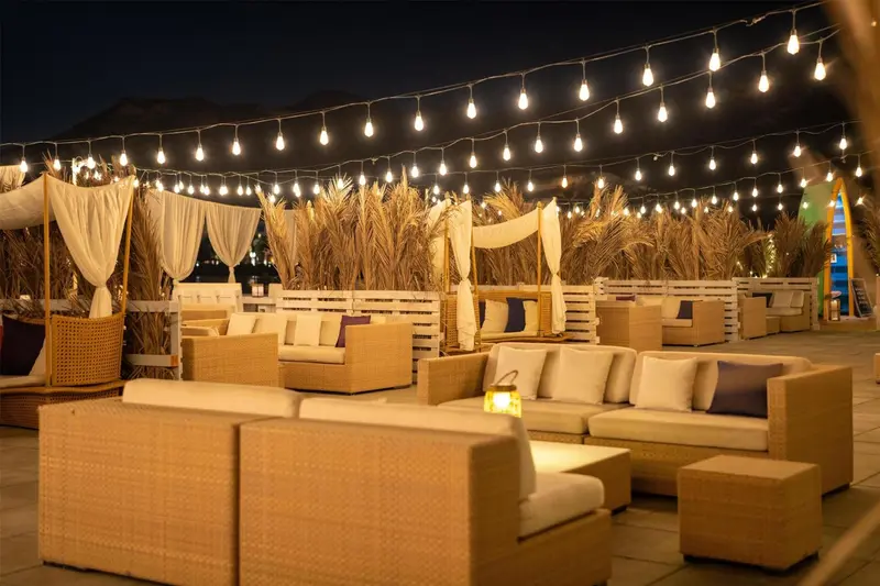 Espace de détente extérieur avec mobilier en rotin et éclairage festif.