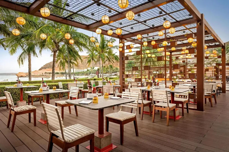 Terrasse ombragée avec tables et chaises en bois près de la mer.